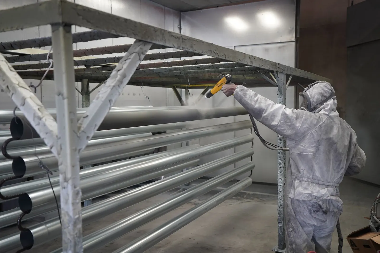 Pintor aplicando tinta em pó em tubos metálicos pendurados na cabine