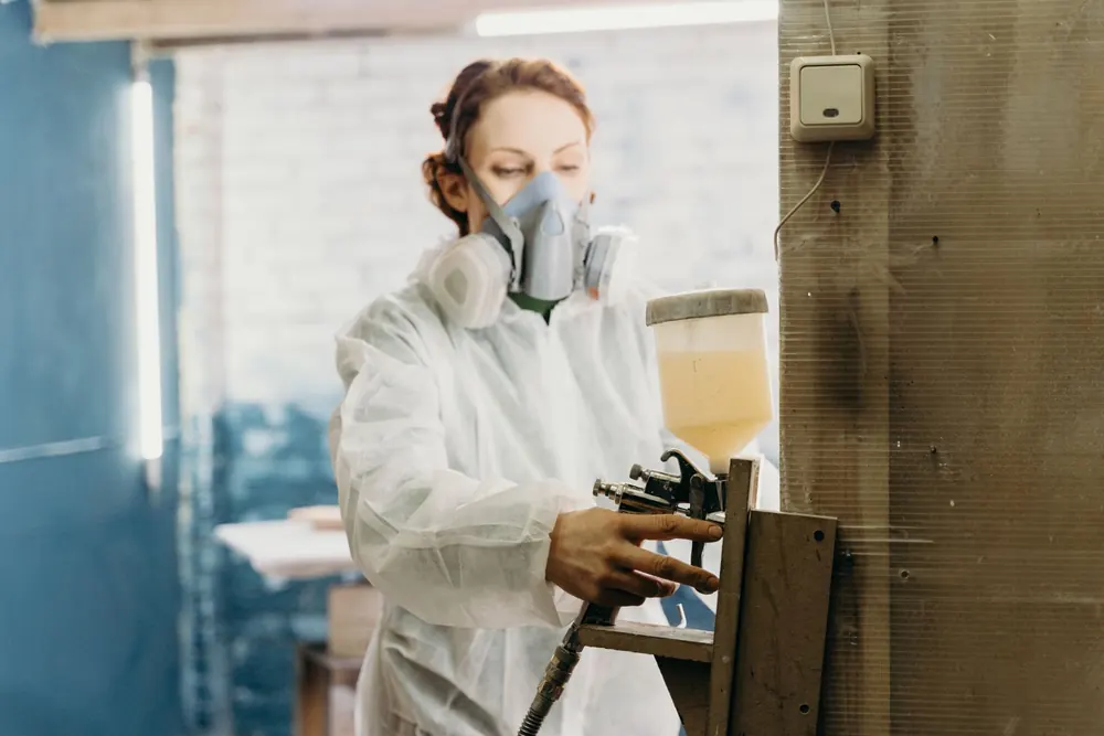 Profissional com máscara e equipamento de proteção usando pistola de pintura